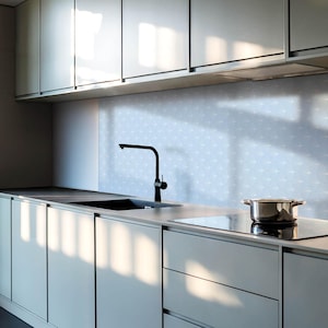 Puede incluir: Una cocina moderna con armarios grises, un grifo negro, un fregadero de acero inoxidable y una placa de cocción negra. El salpicadero es de azulejos de color azul claro con un patrón sutil.