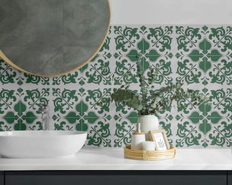 May include: A bathroom vanity area featuring a white oval sink, a round mirror with a thin gold frame, and a wall covered in square tiles with a repeating dark green and white floral pattern. A small white vase with eucalyptus sits on a tray.