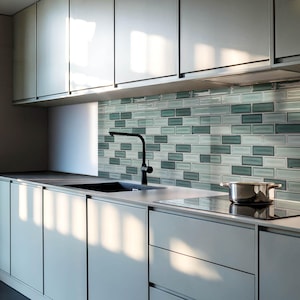 May include: A modern kitchen featuring light gray cabinetry, a black faucet, and a stainless steel pot on a black stovetop. The backsplash is a mosaic of rectangular tiles in shades of blue and gray. The overall design is minimalist and contemporary.