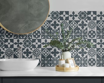 May include: A wall covered in square tiles featuring a repeating dark gray and white geometric floral pattern. The tiles are arranged in a grid, creating a symmetrical design that spans the wall behind a white sink and a round mirror.