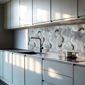 May include: A modern kitchen with gray cabinets and a black faucet. The backsplash is a patterned tile with abstract shapes in shades of gray, pink, and white.