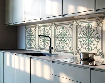 May include: A kitchen backsplash featuring four square tiles with a symmetrical, intricate floral pattern in shades of sage green, soft pink, and dark outlines. The tiles are installed behind a black faucet and a stainless steel cooking pot.