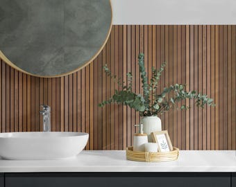 May include: A white oval vessel sink with a chrome faucet sits on a white countertop against a wall with vertical brown wood slats. A round mirror with a gold frame hangs above. A rattan tray holds a white vase with eucalyptus and a small frame.