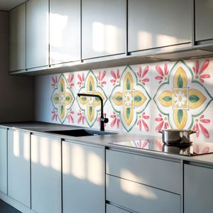 Puede incluir: Una cocina moderna con un protector contra salpicaduras decorativo con un patrón floral repetido en amarillo, verde y rosa. La cocina tiene gabinetes grises, un grifo negro y una olla de acero inoxidable en la estufa.