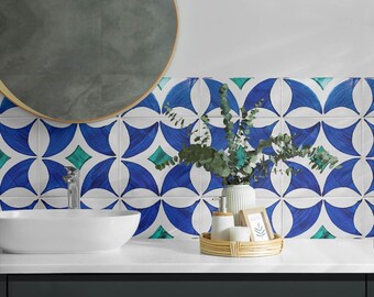 May include: A white oval bathroom sink with a silver faucet sits on a dark countertop against a wall covered in square tiles featuring a repeating blue and white geometric pattern with small green diamond accents and a round mirror above.