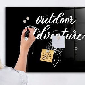 Könnte beinhalten: Ein schwarzes Glas-Whiteboard mit dem Text "outdoor adventure" in weißer Kursivschrift. Das Board hat ein weißes geometrisches Design mit einer Glühbirne und einem Auge. Zwei weiße Haftnotizen sind am Board befestigt.