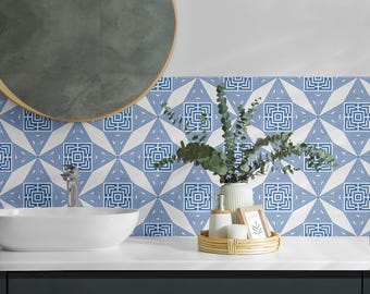 May include: A wall covered in blue and white geometric patterned tiles featuring a repeating square labyrinth design. The wall is positioned behind a white oval vessel sink with a silver faucet and a green plant in a white vase on a counter.
