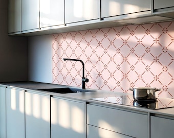 May include: A kitchen backsplash featuring a light pink background with a repeating dark pink diamond grid pattern and small floral accents at each intersection, installed behind a black faucet and a stainless steel cooking pot on a stovetop.