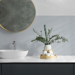 May include: A white ceramic sink with a chrome tap, set against a wall with a light blue chevron patterned tile. A vase with green eucalyptus branches sits on a countertop with a wooden tray holding a white soap dispenser and a picture frame.