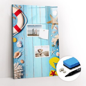 May include: A blue and white magnetic dry erase board with a beach theme. The board features a life preserver, seashells, starfish, and flip flops. There are two photos attached to the board with magnets. The board comes with a dry erase marker and a sponge eraser.
