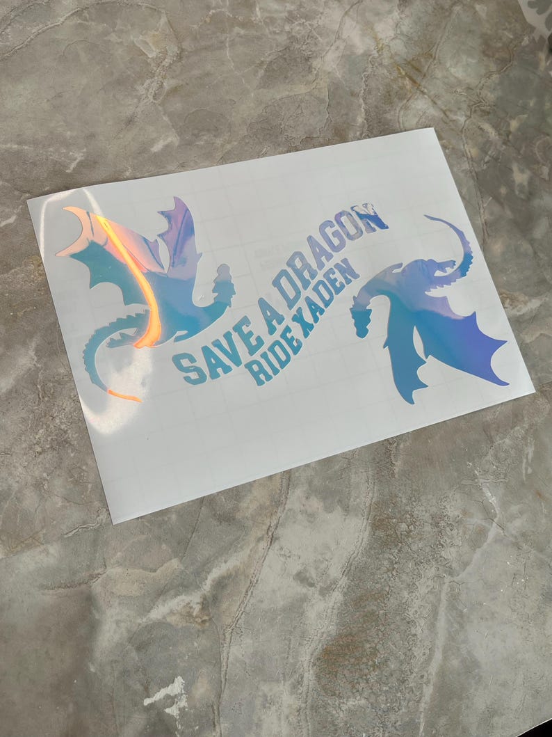 May include: A white sticker with two iridescent blue dragon silhouettes and the text "Save a Dragon Ride a Xaden".