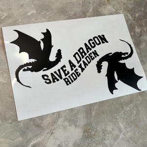 May include: A white sticker with two black dragon silhouettes and the text "Save a Dragon Ride a Kaden".