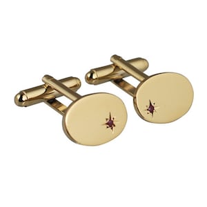 May include: A pair of gold cufflinks with oval-shaped fronts featuring a small red gemstone set in a star design.