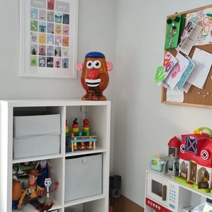 May include: A white bookshelf with toys and books. The top shelf has a Mr. Potato Head toy. The second shelf has a wooden toy stacking tower. The third shelf has a grey storage bin. The fourth shelf has a grey storage bin. The fifth shelf has a toy car. The sixth shelf has a pink storage bin. The bottom shelf has books.