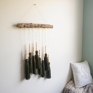 May include: A wall hanging made from a natural branch with green yarn tassels and wooden beads. The tassels are hanging from the branch with string.