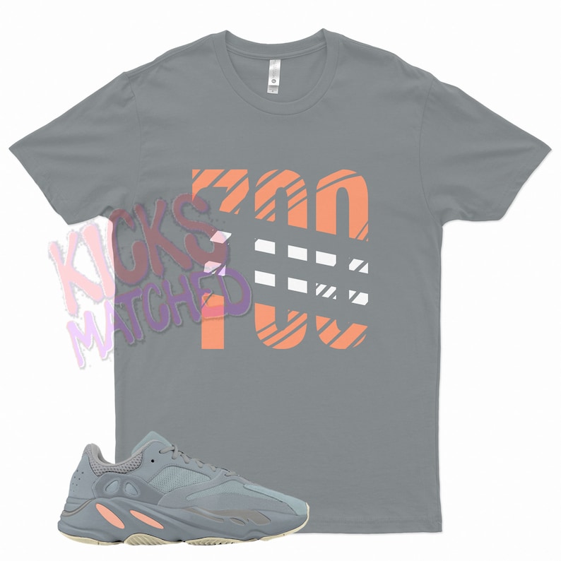 May include: A gray t-shirt with the number 700 printed in orange and white stripes. A pair of gray and cream sneakers are also pictured.