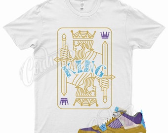 May include: White t-shirt with a gold outline of a king of spades playing card with the word "KING" in blue and purple.  A pair of yellow, purple, and blue sneakers are shown below the shirt.