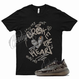 May include: Black t-shirt with a graphic print of a broken heart with the text "Love me not broke heart hurt me".  The shirt is paired with a pair of camouflage sneakers.