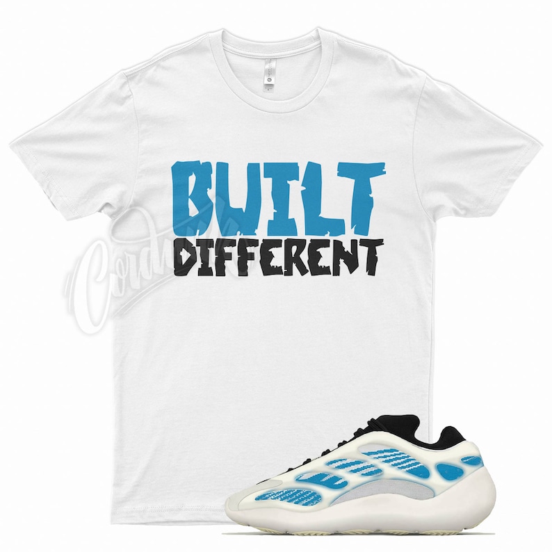 May include: White t-shirt with the text "BUILT DIFFERENT" in blue and black. A pair of white and blue sneakers with a unique design is displayed below the shirt. The sneakers have a thick sole and a modern aesthetic.