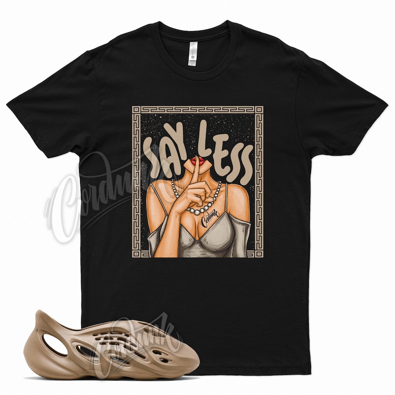 May include: A black t-shirt with a graphic of a woman with her finger to her lips and the text "Say Less" in a gold frame. The t-shirt is paired with a pair of tan foam clogs.