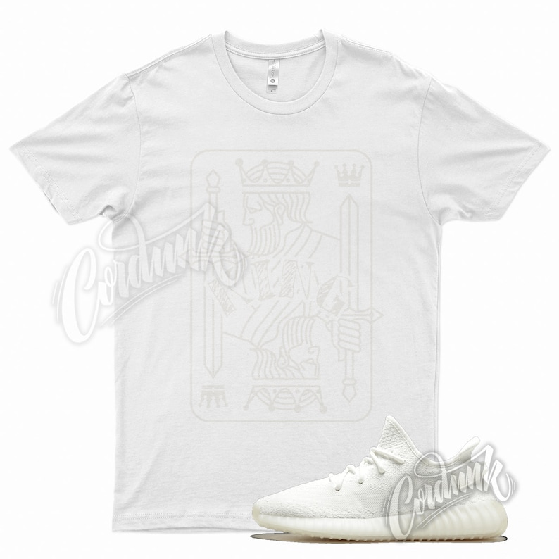 May include: White t-shirt with a white outline of the King of Spades playing card. A pair of white sneakers with a cream sole.