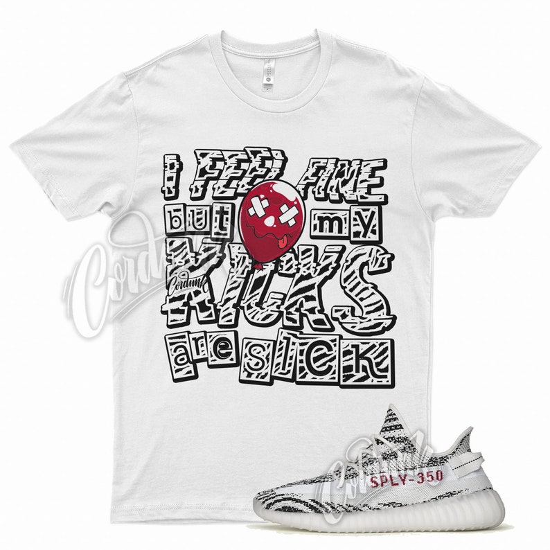 May include: White t-shirt with black and white zebra print text that reads "I feel fine but my kicks are sick". A red balloon with a bandage and a tongue sticking out is in the middle of the text. A pair of white and black zebra print sneakers with red accents are below the t-shirt.