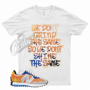 May include: White t-shirt with the text "WE DON'T GRIND THE SAME SO WE DON'T SHINE THE SAME" in orange, blue, and black. A pair of orange, blue, and gray sneakers is in the foreground.