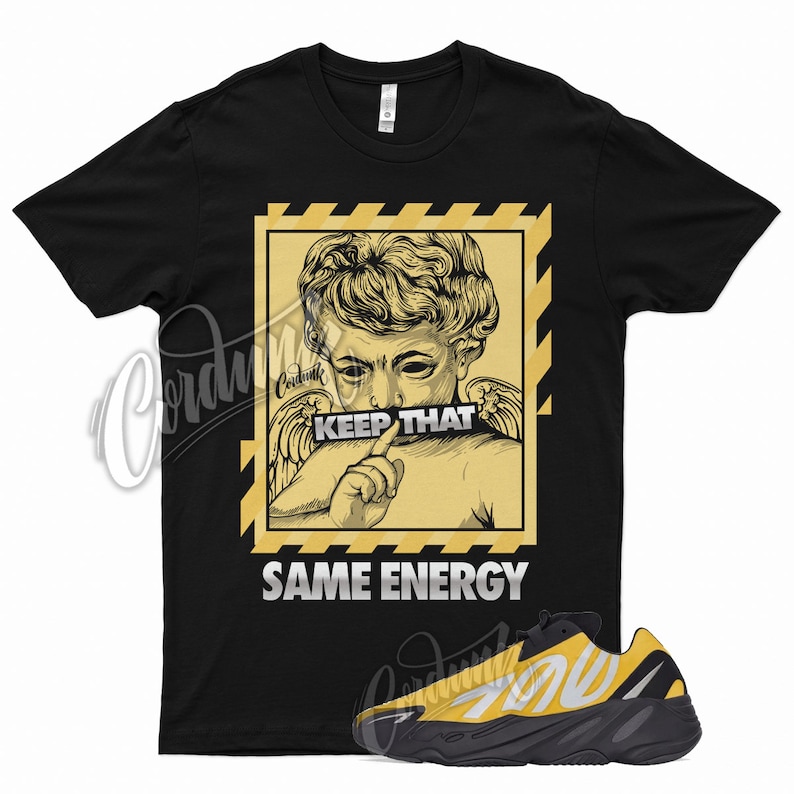 May include: Black t-shirt with a yellow graphic of a cherub with the text "Keep That Same Energy".  A pair of black and yellow sneakers are shown below the t-shirt.