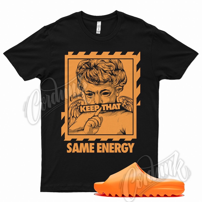 K&ouml;nnte beinhalten: Schwarzes T-Shirt mit einem orangefarbenen Aufdruck einer klassischen Statue und dem Text "KEEP THAT SAME ENERGY". Eine orangefarbene Badesandale befindet sich im Vordergrund.
