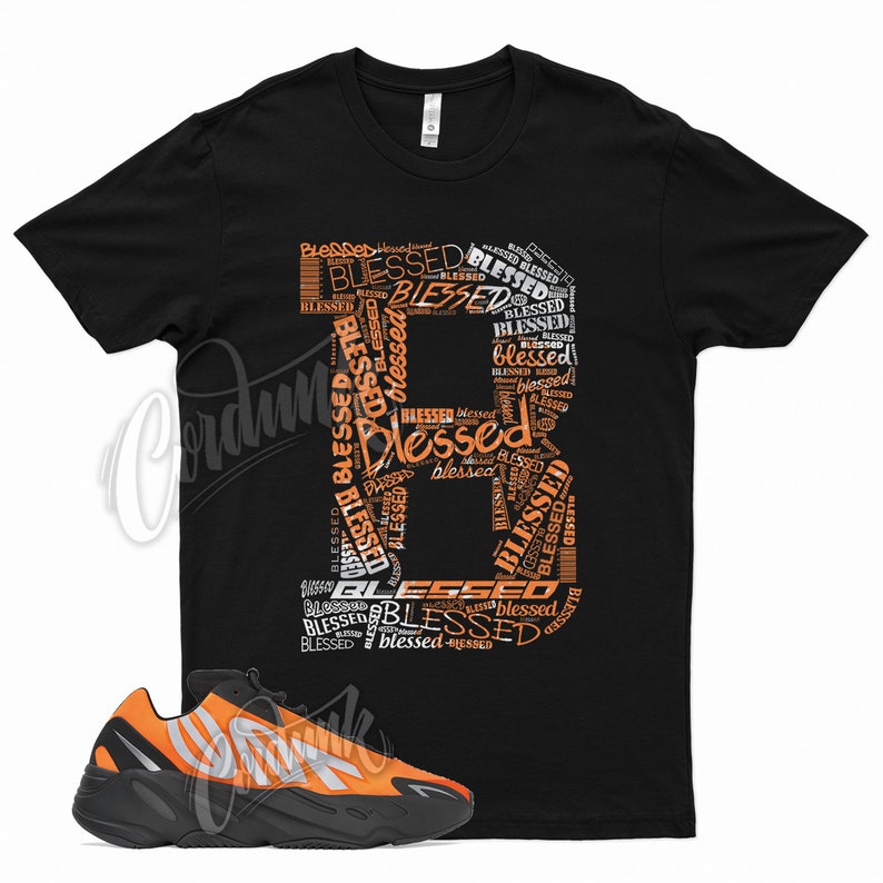 May include: Black t-shirt with an orange and white graphic of the word "Blessed" repeated in a stylized font. A pair of black and orange sneakers are shown below the t-shirt.
