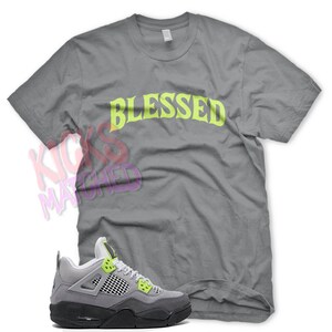 May include: Gray t-shirt with the word "Blessed" in neon green lettering.  Gray and black Air Jordan 4 sneakers with neon green accents.