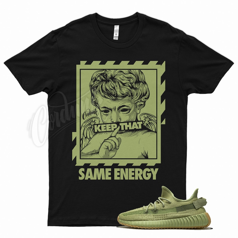 May include: Black t-shirt with a green graphic of an angel figure with the text "KEEP THAT SAME ENERGY." A pair of green sneakers is displayed below the shirt. The shirt and shoes are on a white background.