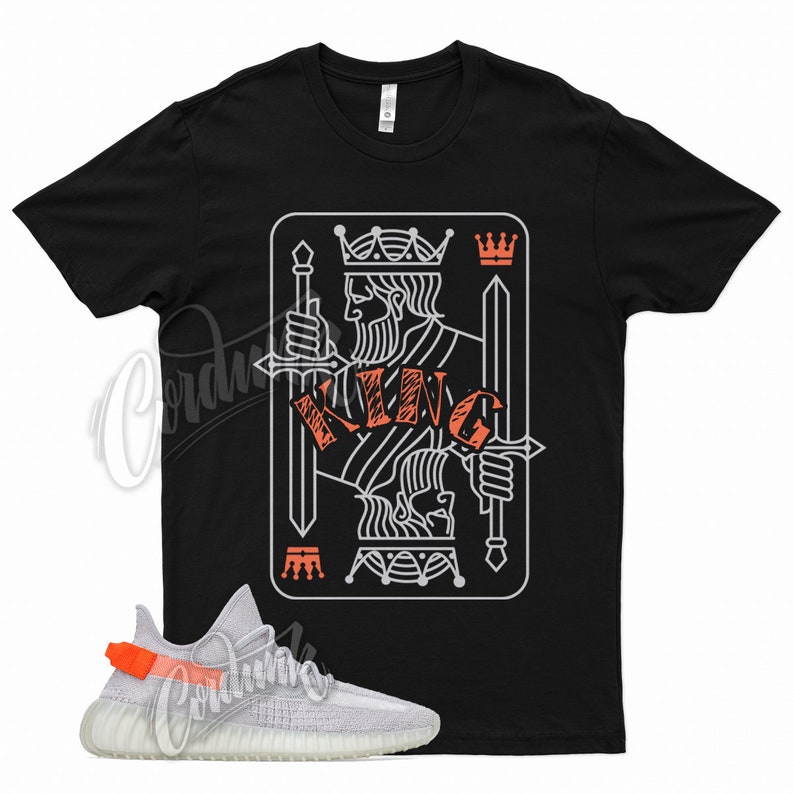 May include: Black t-shirt with a white outline of a king of spades playing card with the word "KING" written in orange. A pair of white and orange sneakers are in the bottom left corner of the image.
