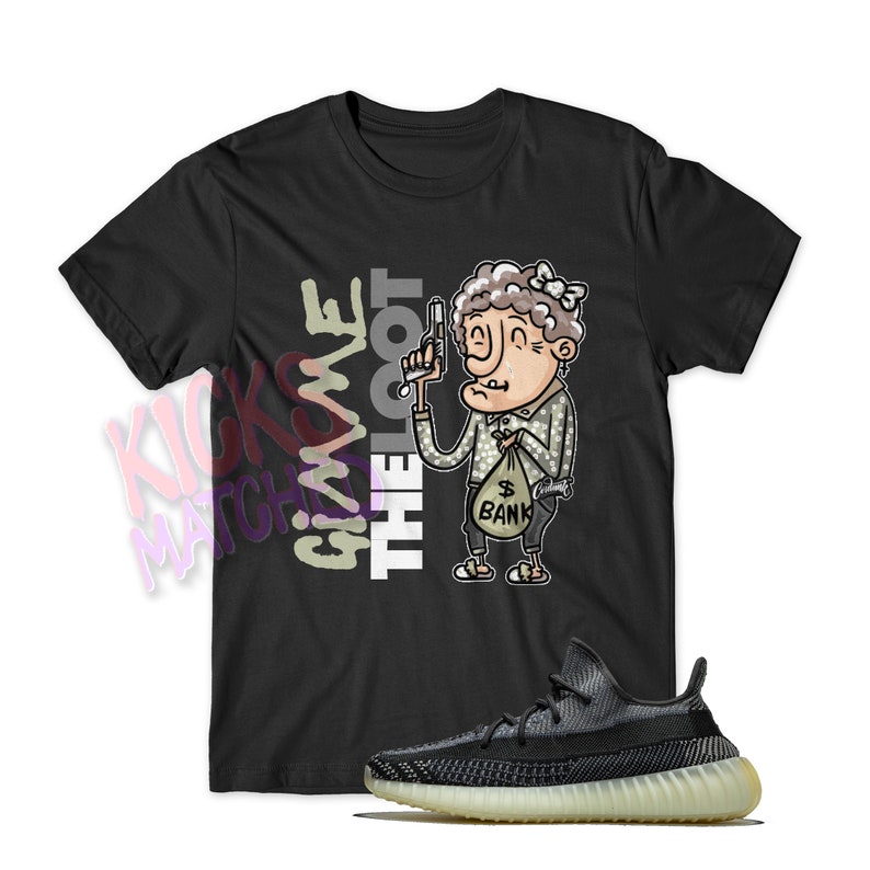 May include: Black t-shirt with a cartoon illustration of a woman holding a gun and a bag of money. The text "Give me the loot" is printed on the shirt. A pair of black and white sneakers with a light brown sole are also pictured.