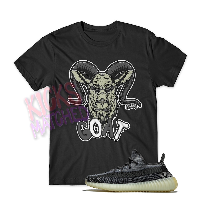 May include: Black t-shirt with a goat graphic and the word "GOAT" in white and gray. A pair of black and gray sneakers with a light yellow sole are displayed below the shirt.