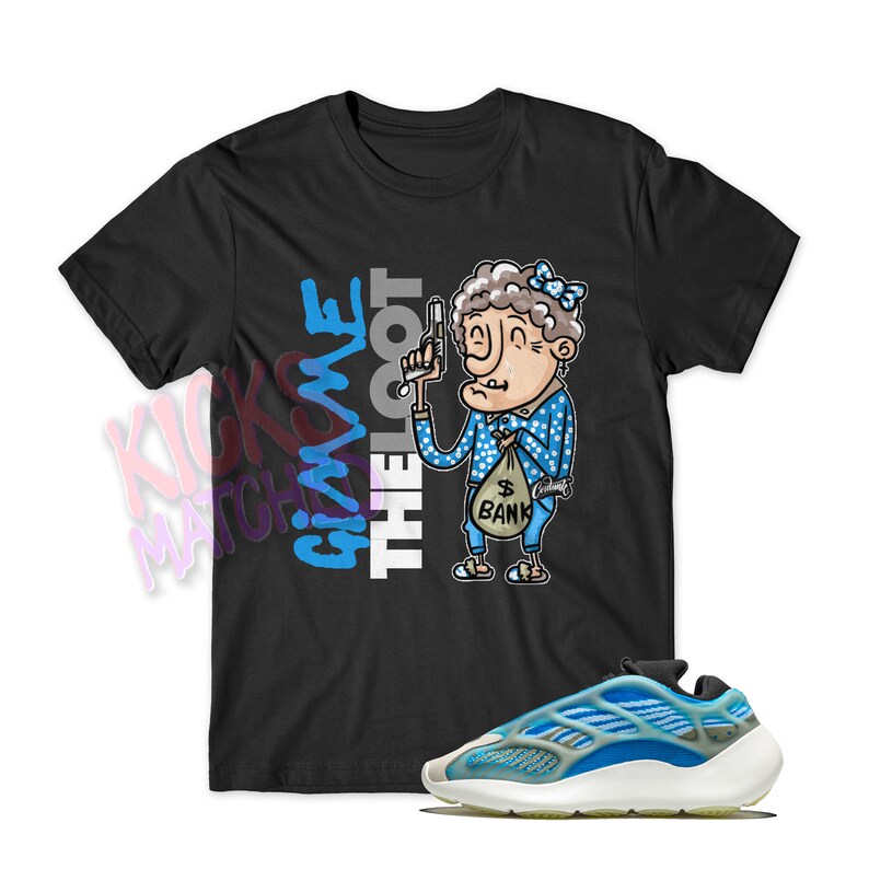 Puede incluir: Camiseta negra con una ilustraci&oacute;n de dibujos animados de una mujer sosteniendo un arma y una bolsa de dinero. El texto "Give me the loot" est&aacute; impreso en la camiseta. Tambi&eacute;n se muestra un par de zapatillas azules y blancas.