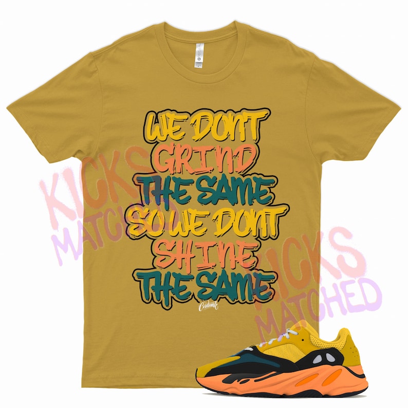 May include: A mustard yellow t-shirt with the text "We don't grind the same so we don't shine the same" in colorful graffiti-style lettering. A pair of yellow, black, and orange sneakers are also pictured.