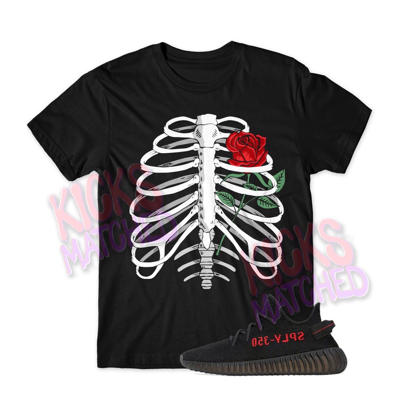 Op de afbeelding: Zwart T-shirt met een wit ribbenkastontwerp en een rode roos. Een zwarte en bruine sneaker met rode tekst staat ook op de afbeelding. De shirt en sneaker vormen waarschijnlijk een bijpassende set.