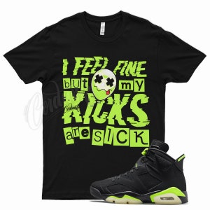 May include: Black t-shirt with a green graphic that says "I feel fine but my kicks are sick". A pair of black and green sneakers are shown below the t-shirt.