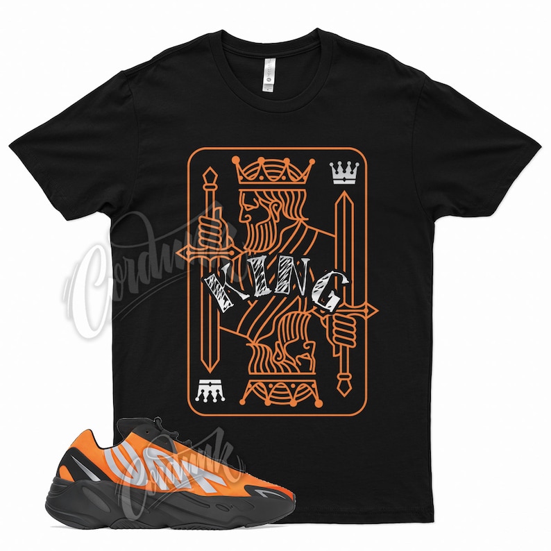 Puede incluir: Una camiseta negra con un gr&aacute;fico de la carta de juego rey de picas naranja. La camiseta se combina con zapatillas de deporte naranja y negras.