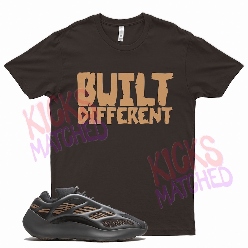 May include: A brown t-shirt with the text "BUILT DIFFERENT" in tan lettering. A black and tan sneaker is shown below the t-shirt.