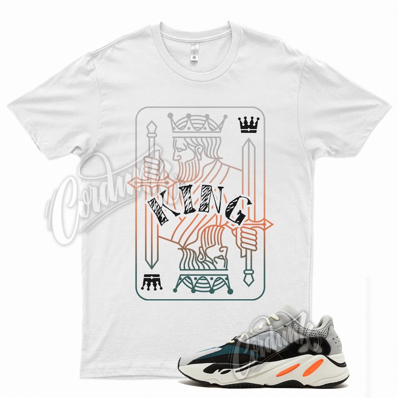May include: White t-shirt with a graphic of a king of spades playing card with the word "KING" in the center.  The graphic is in a gradient of orange, green, and blue.  A pair of white, black, and orange sneakers are shown below the t-shirt.