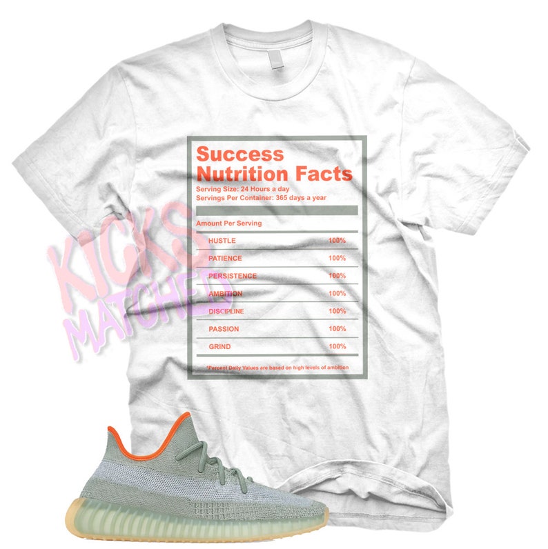May include: A white t-shirt with a nutrition facts label that says "Success Nutrition Facts" with the following ingredients: Hustle, Patience, Persistence, Ambition, Discipline, Passion, and Grind. Each ingredient is listed as 100%. The t-shirt is paired with a pair of light green and orange sneakers.