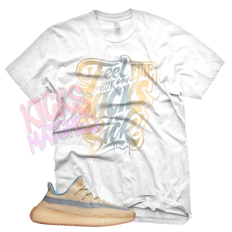 May include: White t-shirt with the text "Feel fine but my kicks are sick" in gold and blue lettering. A pair of light blue and beige sneakers are shown below the t-shirt.