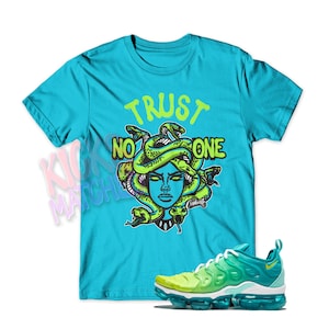 May include: A turquoise blue t-shirt with a green and yellow graphic of a Medusa head with snakes and the text "TRUST NO ONE". A pair of green and yellow Nike VaporMax sneakers are also pictured.
