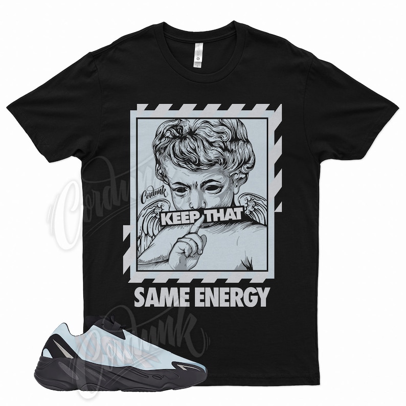 May include: Black t-shirt featuring a graphic of a cherub with the text "KEEP THAT SAME ENERGY." Below the shirt is a black and light blue sneaker.