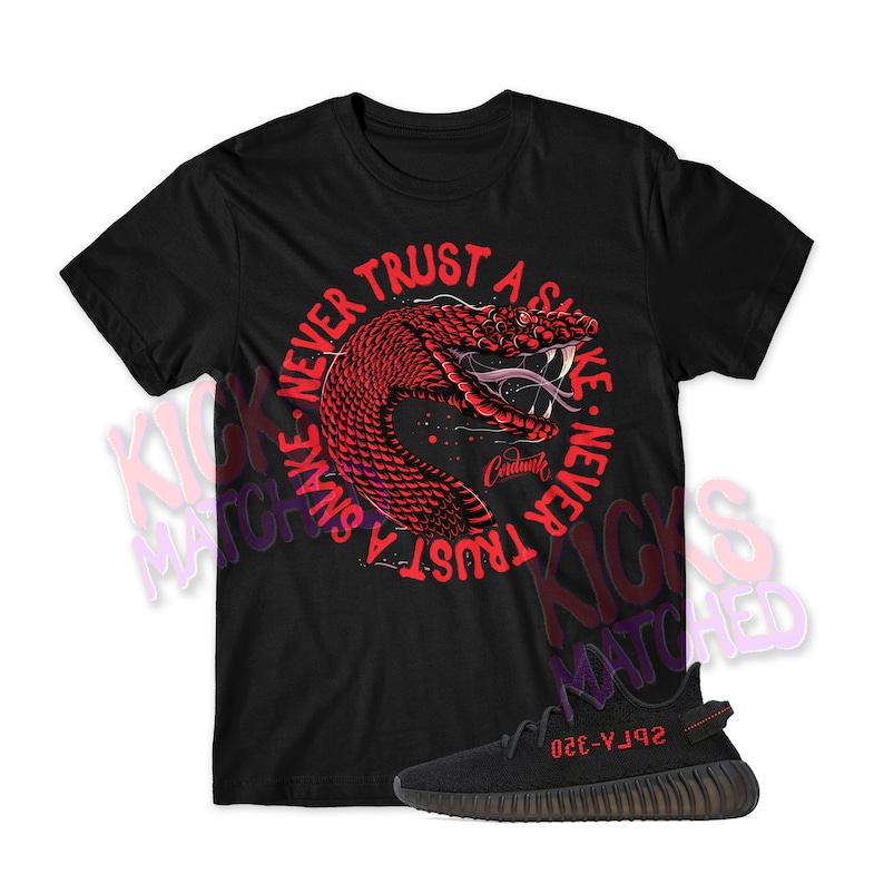 Puede incluir: Camiseta negra con un gr&aacute;fico de serpiente roja y el texto "Never Trust A Snake. Never Trust A Snake." La camiseta se combina con zapatillas negras con detalles rojos y el texto "Yeezy 350" en el lateral.