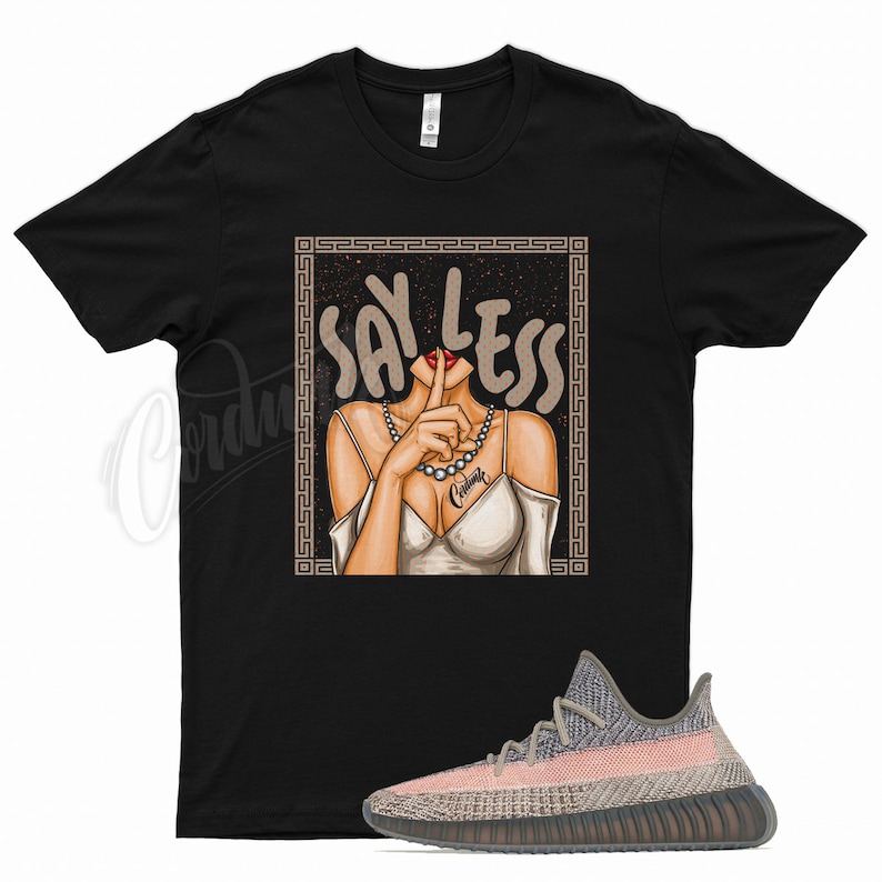 Peut inclure: T-shirt noir avec un motif repr&eacute;sentant une femme se tenant le doigt sur les l&egrave;vres et le texte "Say Less". La femme porte une robe blanche et un collier de perles. Le motif est entour&eacute; d'un cadre dor&eacute;. Une paire de baskets roses et grises est &eacute;galement repr&eacute;sent&eacute;e.