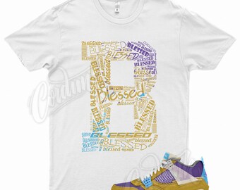 May include: A white t-shirt with a graphic design of the word "Blessed" repeated in a variety of fonts and colors. The graphic is in the shape of the number "4". A pair of yellow, purple, and blue sneakers are shown below the t-shirt.
