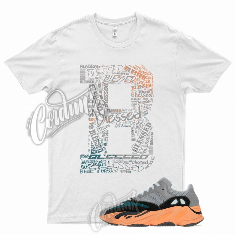 May include: White t-shirt with a graphic design of the word "blessed" repeated in different sizes and colors, forming the shape of a peace sign. The shirt is paired with a pair of orange and grey sneakers.